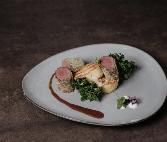 Pink roasted saddle of venison wrapped in herbs with greens