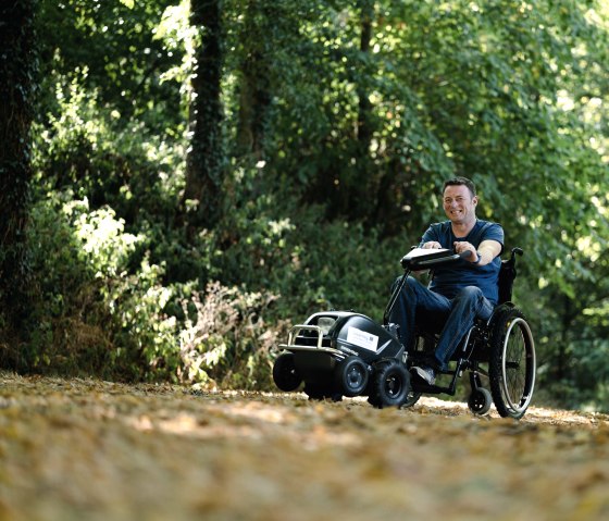 Rollstuhlfahrer mit Rollstuhlzuggerät auf einem Wanderweg im Naturpark Südeifel, © Naturpark Südeifel, Thomas Urbany