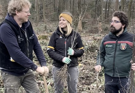 Unter der Leitung von Förster Julian Gröber haben viele Freiwillige bei der Baumpflanzaktion in Ernzen geholfen. (v. l. n. r.: Bruno Zwank und Anna Carina Krebs (Geschäftsführer und Tourismusmanagerin der Felsenland Südeifel Tourismus GmbH), Julian Gröber (Revierförster)., © Felsenland Südeifel Tourismus GmbH